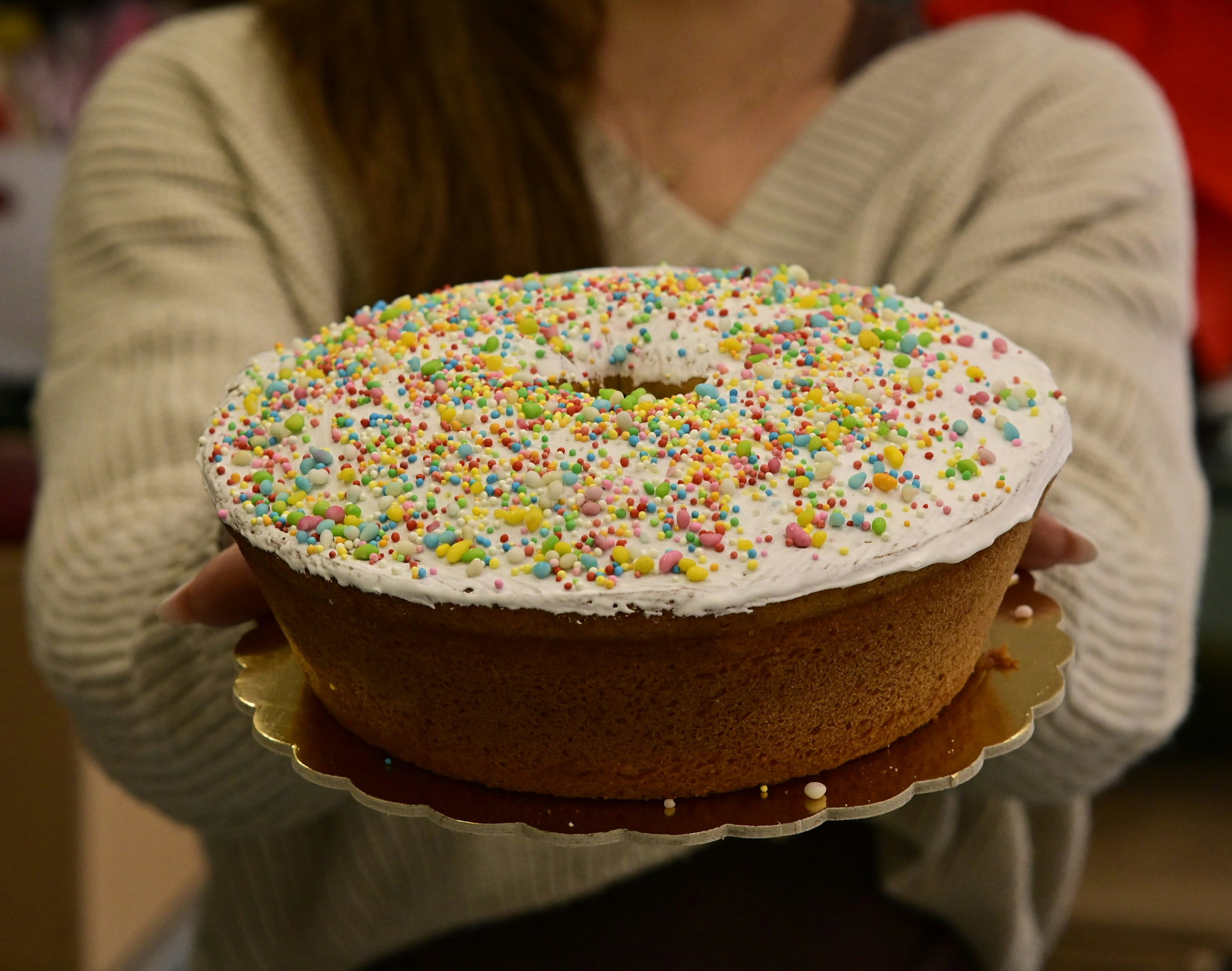 person-holding-a-bundt-cake-with-white-frosting-and-sprinkles.jpg Person holding a bundt cake with white frosting and sprinkles